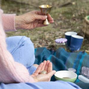 Hand met brandend kaarsje op een kleed in de natuur, een moment van reflectie en innerlijke vrede volgens de Ayurvedische benadering van Annelies Lammers