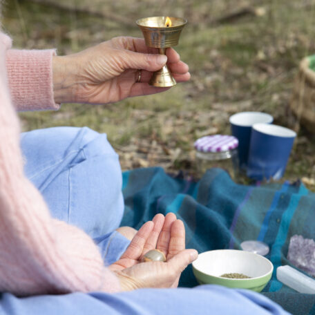 Hand met brandend kaarsje op een kleed in de natuur, een moment van reflectie en innerlijke vrede volgens de Ayurvedische benadering van Annelies Lammers